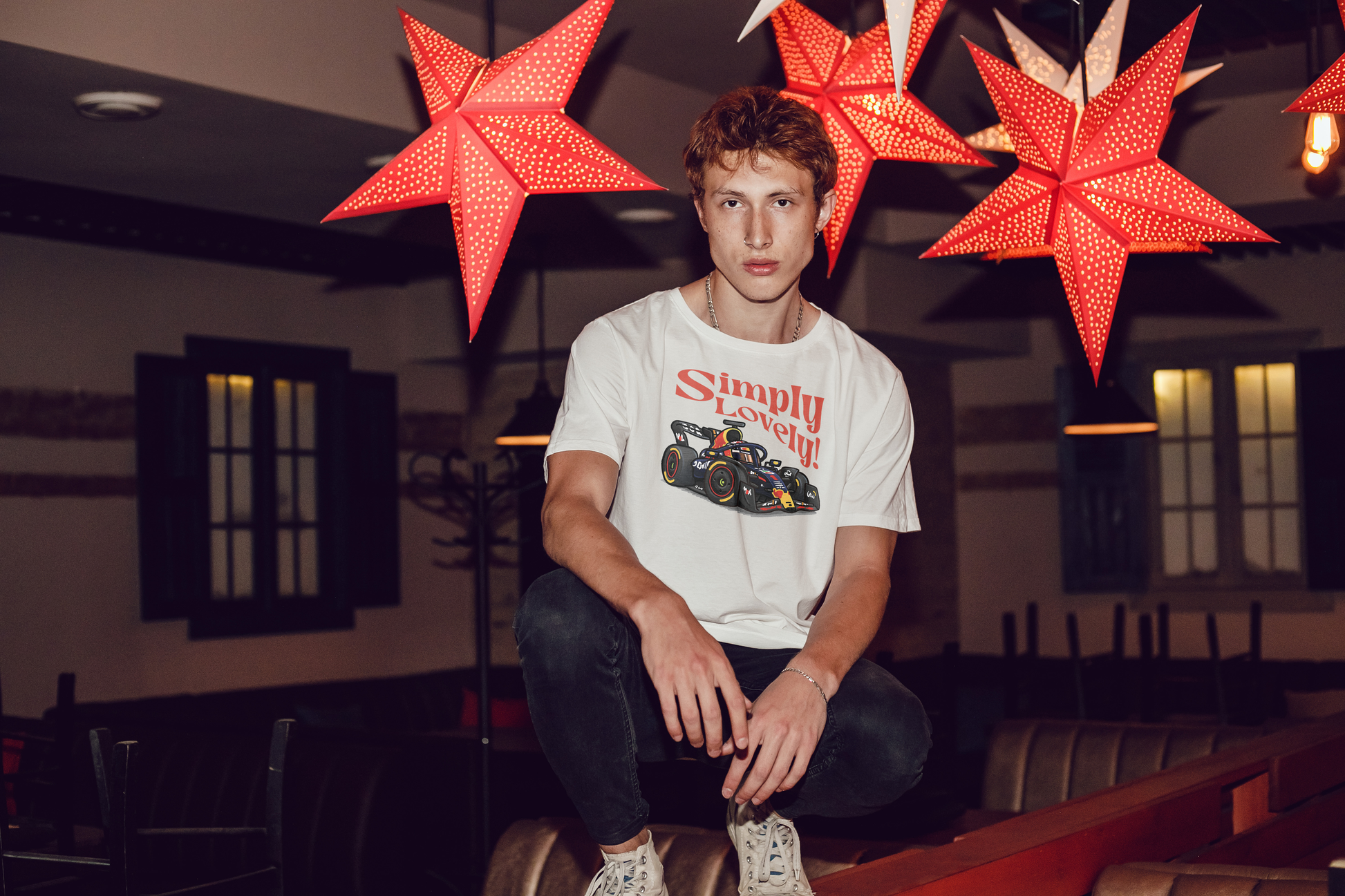 Person wearing a white t-shirt with a graphic design sitting in a room with red star-shaped lights.